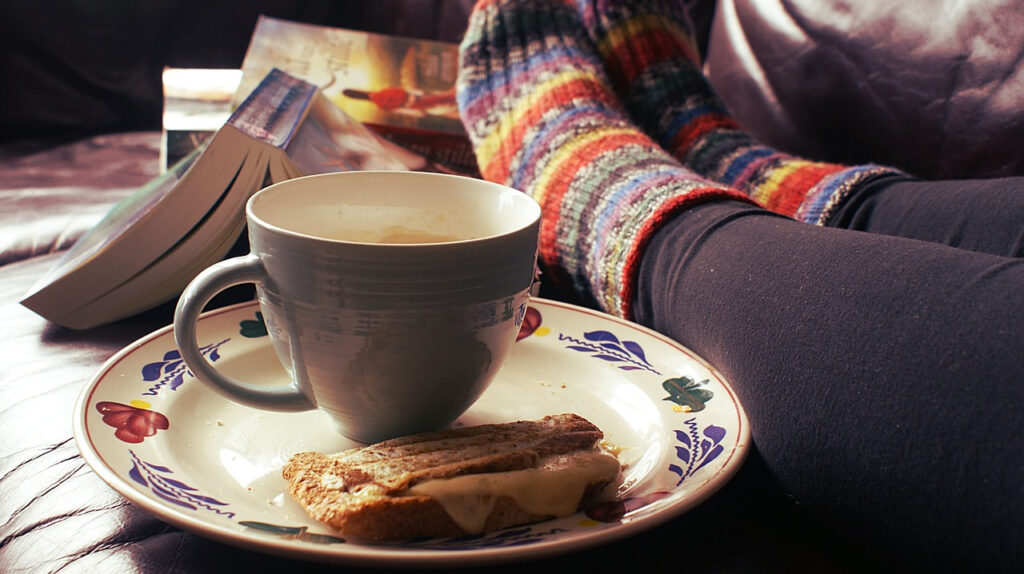 Person with feet up, bright socks, coffee cup, toast, book